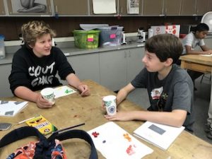 Two students sitting at a table with different colored jelly beans in front of them on the table, each holding their own cup.