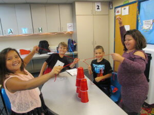 Students pull on strings attached to solo cups to stack them in a tower.