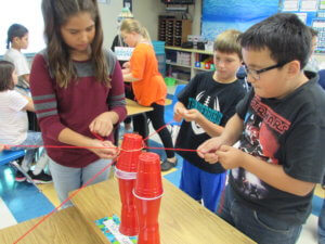 Students pull on strings attached to solo cups to stack them in a tower.