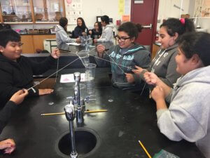 Students use strings and elastics to try to stack cups on top of each other.