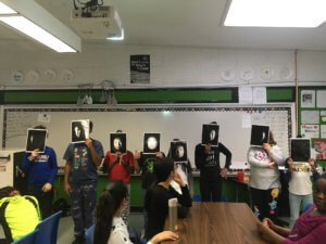 Students stand at the front of the class holding pictures of a face depicting the phases of the moon.