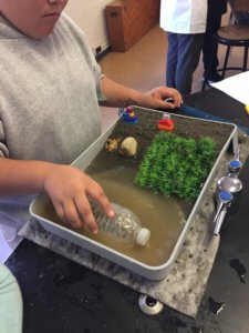 A student uses a water bottle to create waves in a model beach.