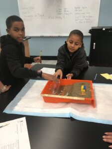 Students create waves with a water bottle in a model beach.