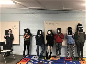 Students hold up photos of a face modeling the phases of the moon.