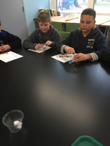 Students investigate dry ice in cups by pressing a metal spoon against the dry ice.