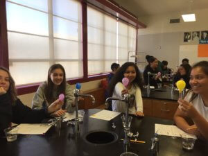 Students sitting at a lab table hold up test tubes with dry ice and balloons on top.