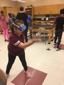 A student wearing goggles throws at a bean bag.