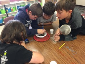 Students use a magnet in a mixture over a plastic bowl, sitting on a plate.