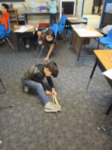 Students measure a rope on the floor with a ruler.