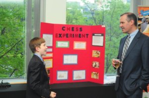 Student showing his science fair board at the gala to an adult.