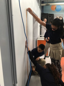 Students use a measuring tape against the wall.