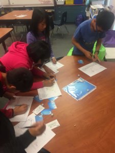 Students roll dice and read cards as part of the Water Cycle game.